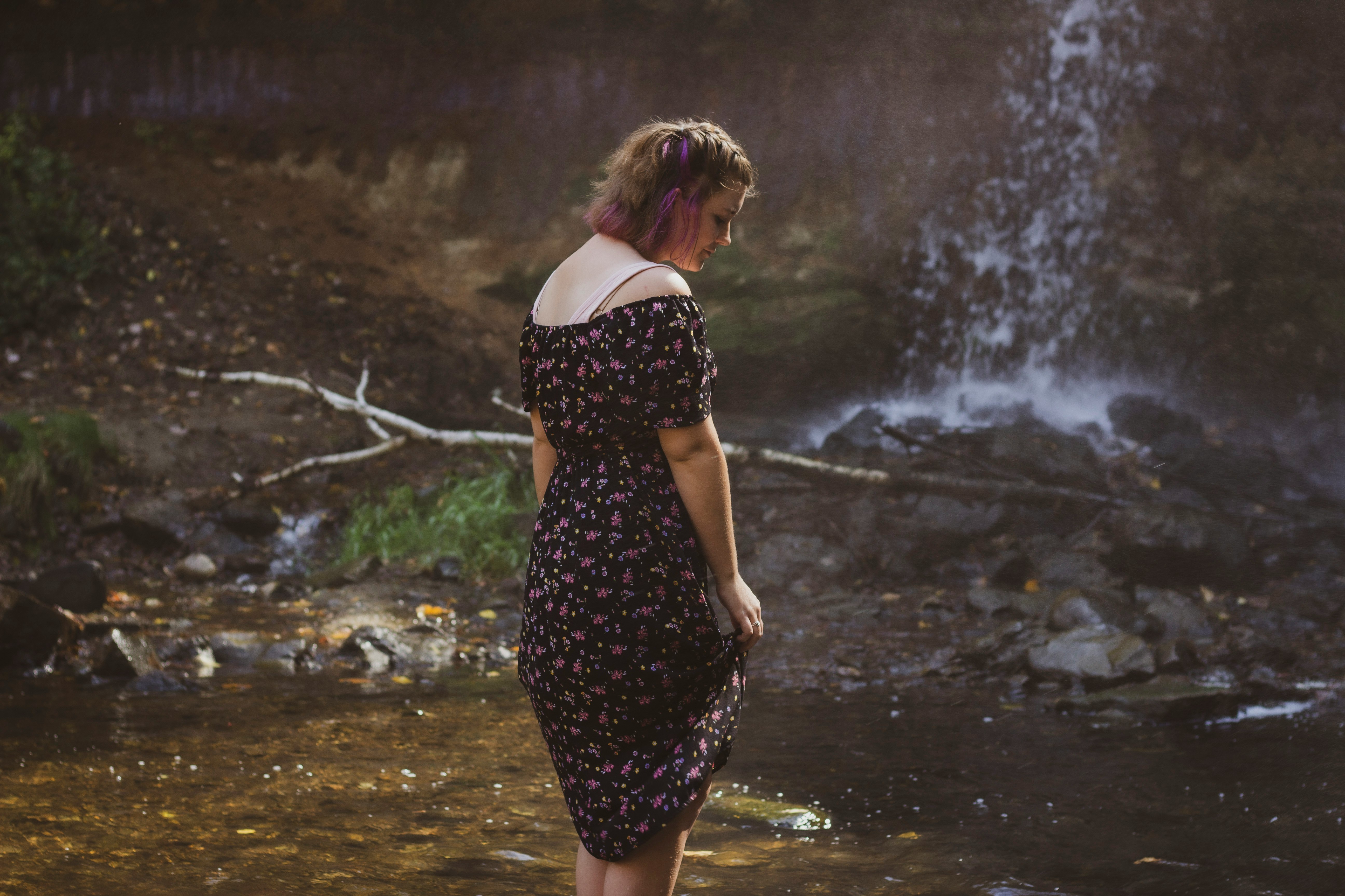 woman in black and white floral dress standing on water falls